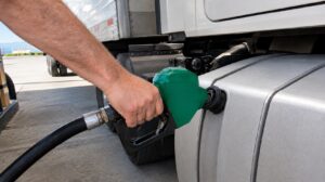 A hand pumping diesel fuel into a semi truck with a dry van trailer, representing rising diesel costs and fuel surcharges on food and beverage packaging shipments in 2026
